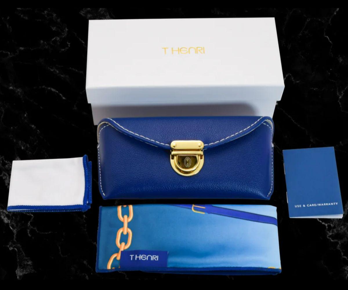 Blue handbag with gold lock, white box, and accessories on a dark background