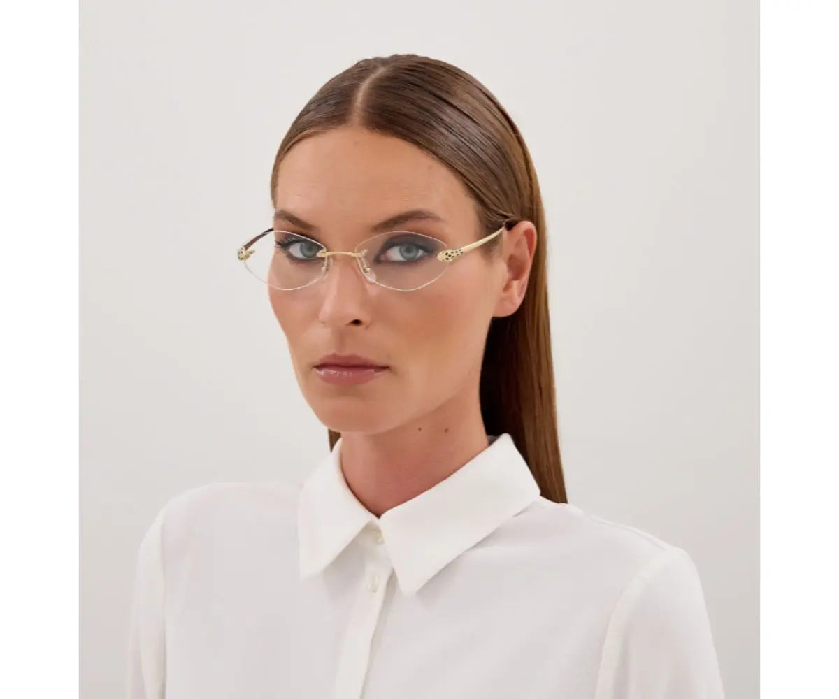 Woman wearing gold-framed glasses and a white shirt against a light gray background